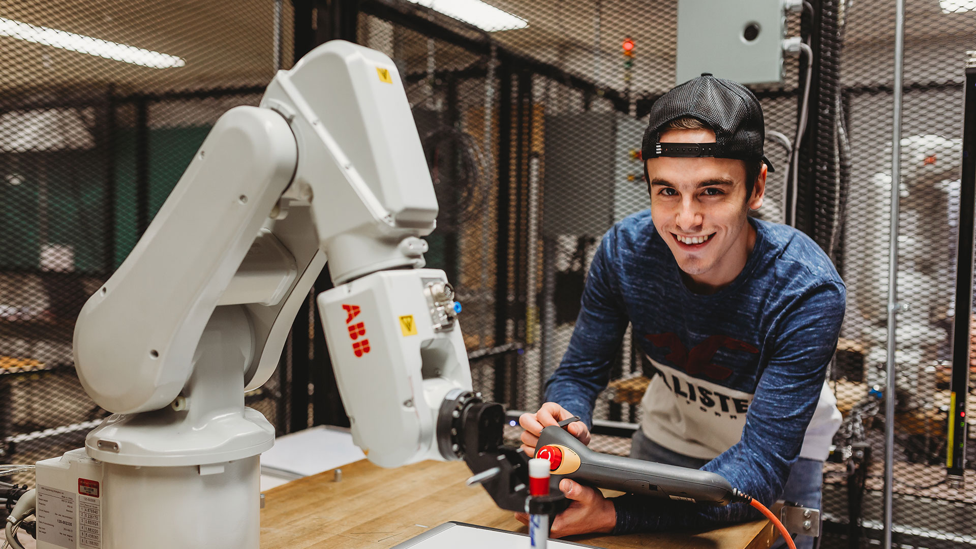 Étudiant souriant à la caméra manipulant un bras robotique