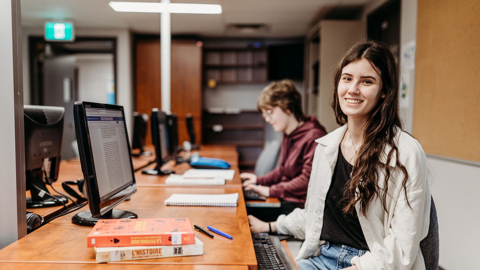 Une jeune femme souriant à la caméra devant un ordinateur.