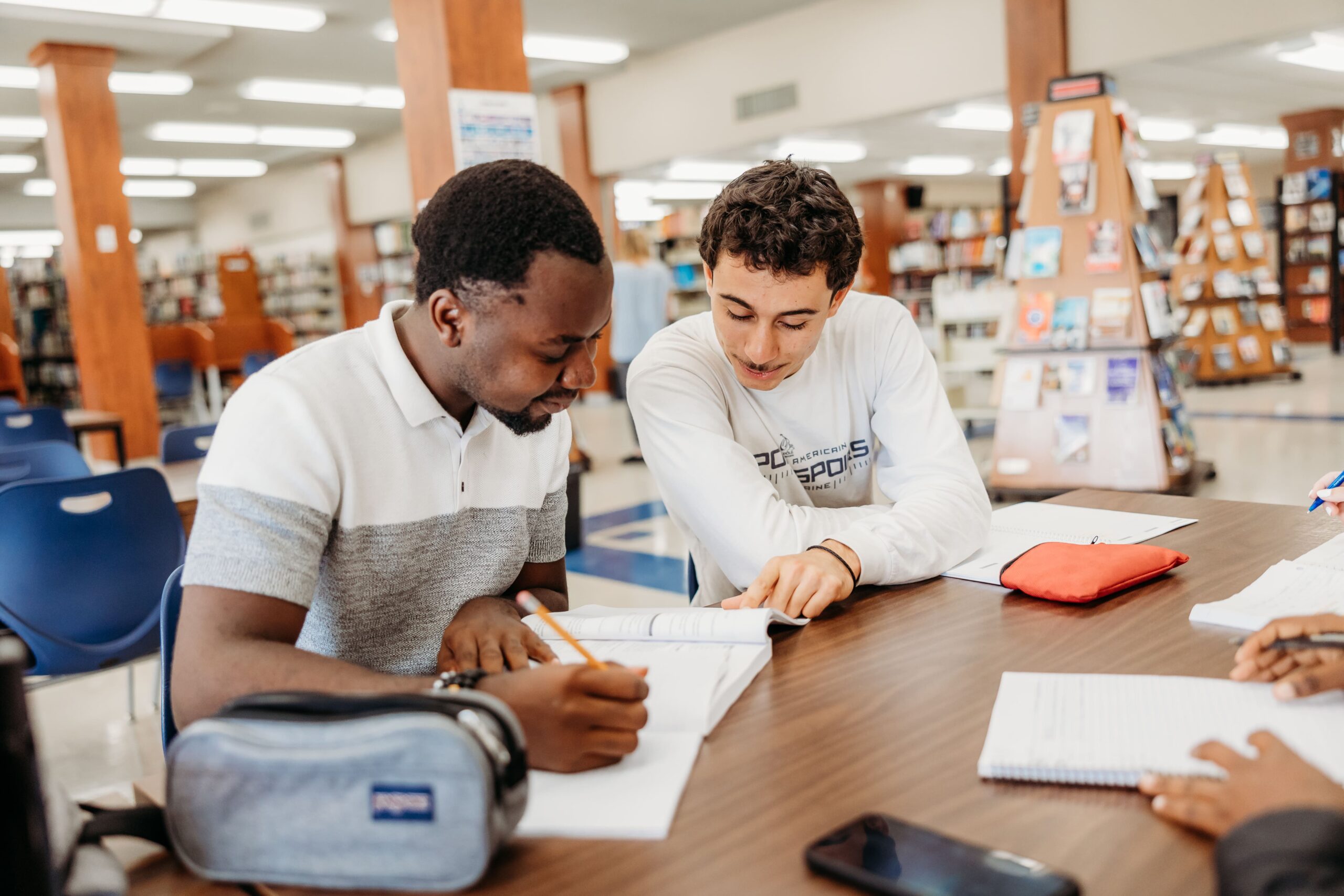 Deux étudiants consultent un ouvrage dans une bibliothèque.