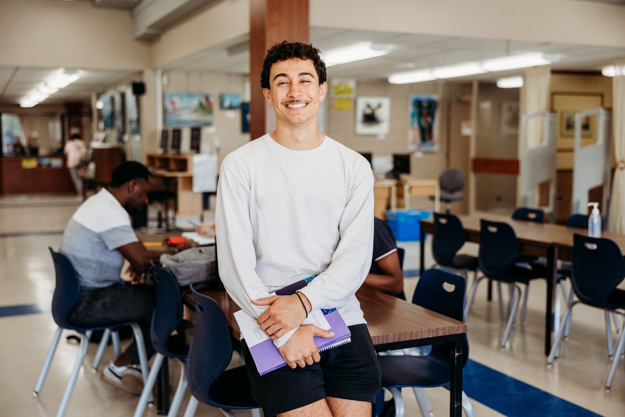 Étudiant souriant à la caméra dans un espace commun.