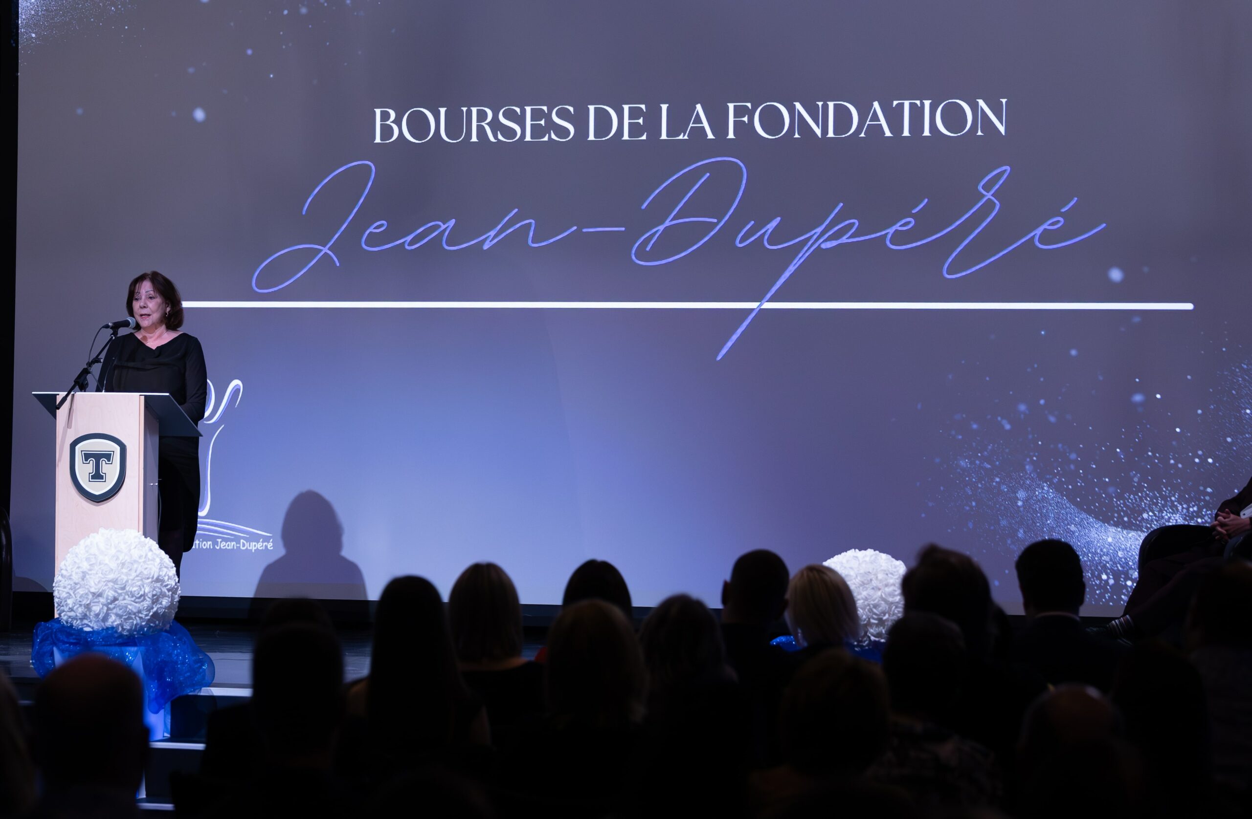 Une femme s'adresse à une salle bondé lors d'un événement des bourses de la fondation Jean-Dupéré, avec un podium avec le logo du Cégep de Thetford.