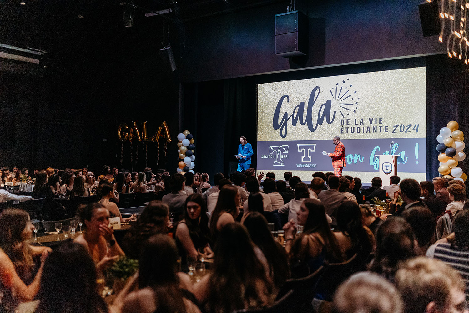 Photo en plan large d'un événement de gala de la vie étudiante 2024 du Cégep de Thetford. La salle est bondée et des présentateurs s'adressent à la foule.