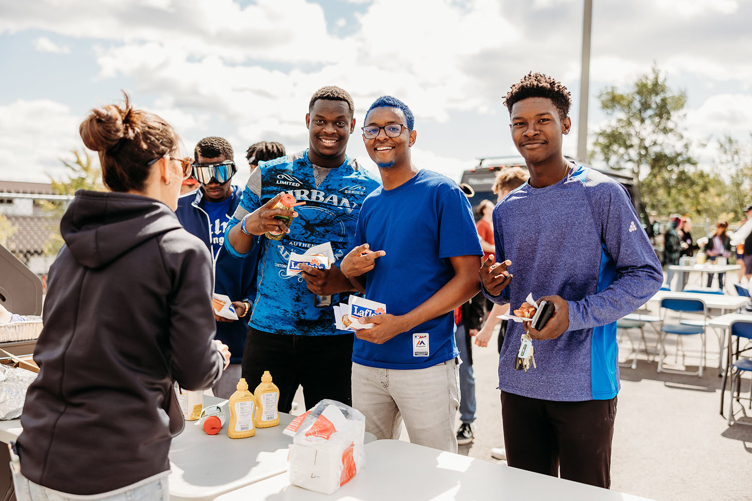 Photo de trois étudiants souriants à la caméra lors d'un barbecue à l'extérieur dans le contexte d'un événement social.