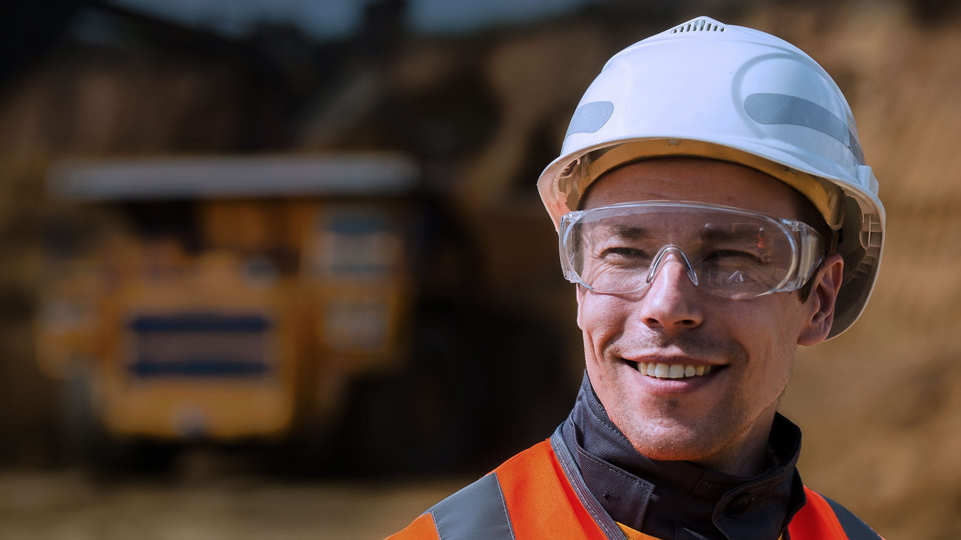 Étudiant souriant à la caméra avec des lunettes et un casque de protection.