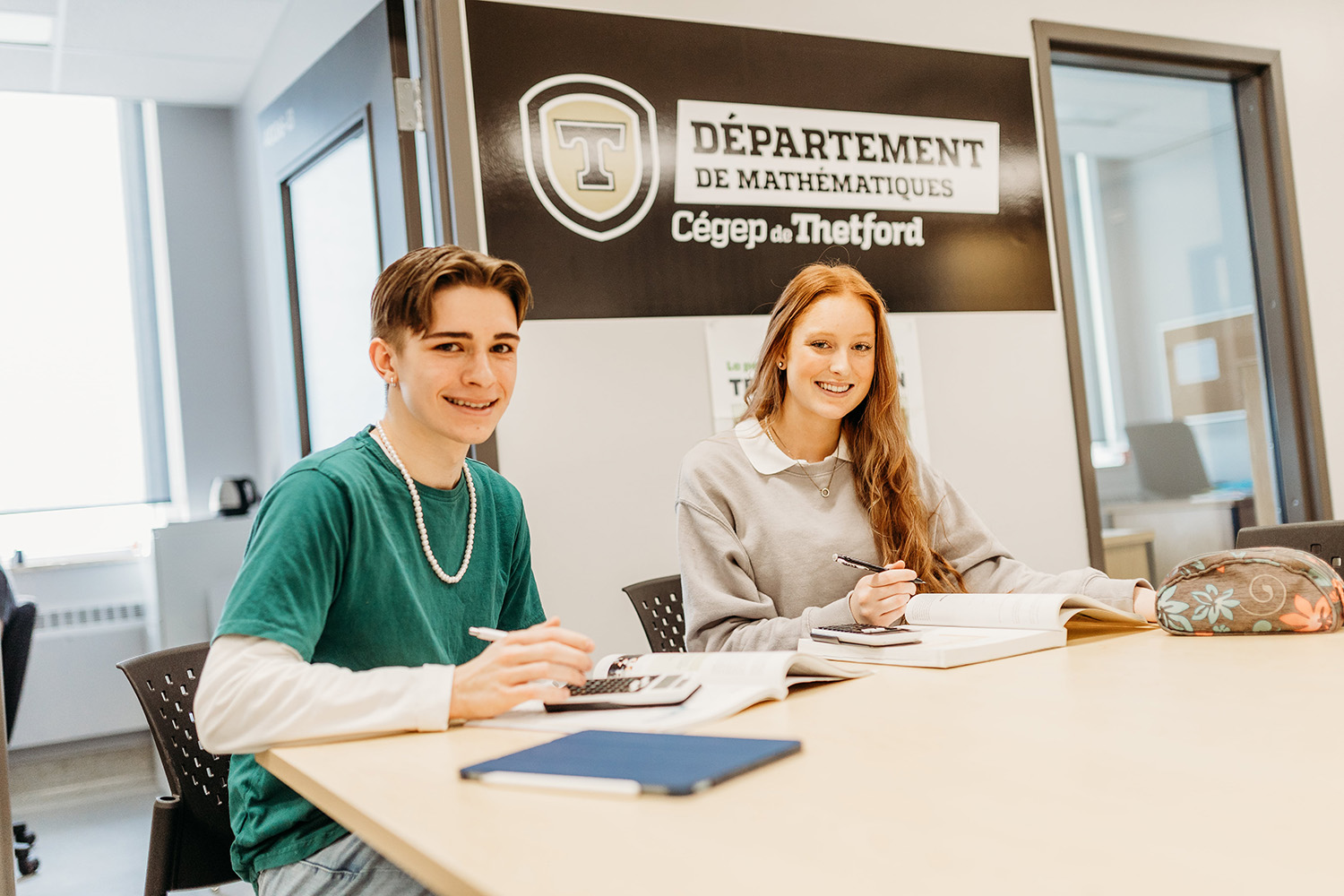 Photo de deux étudiants souriants à la caméra alors qu'il étudient dans une salle du département de mathématiques du Cégep de Thetford.