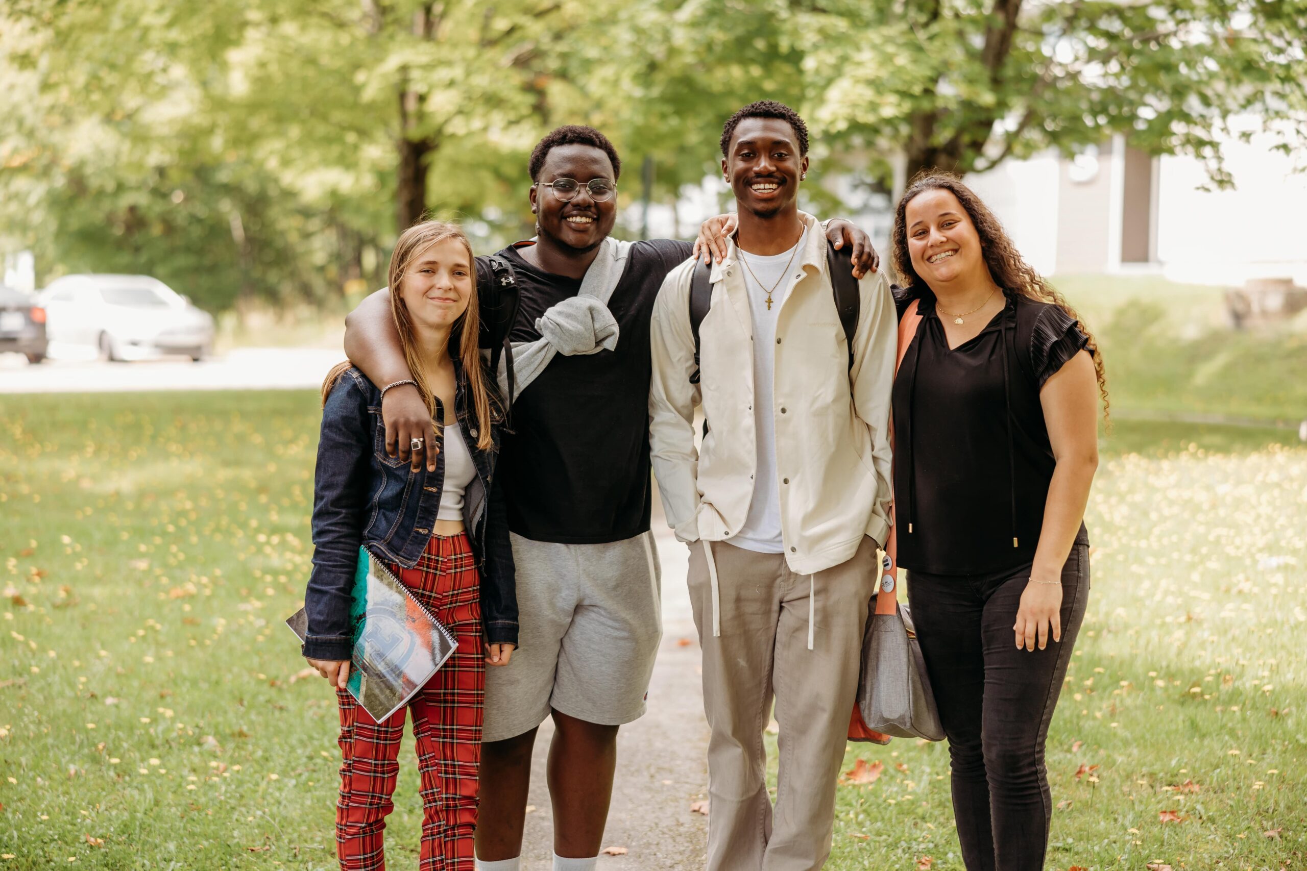Une photo de groupe de quatre jeunes étudiants souriant à la caméra à l'extérieur.