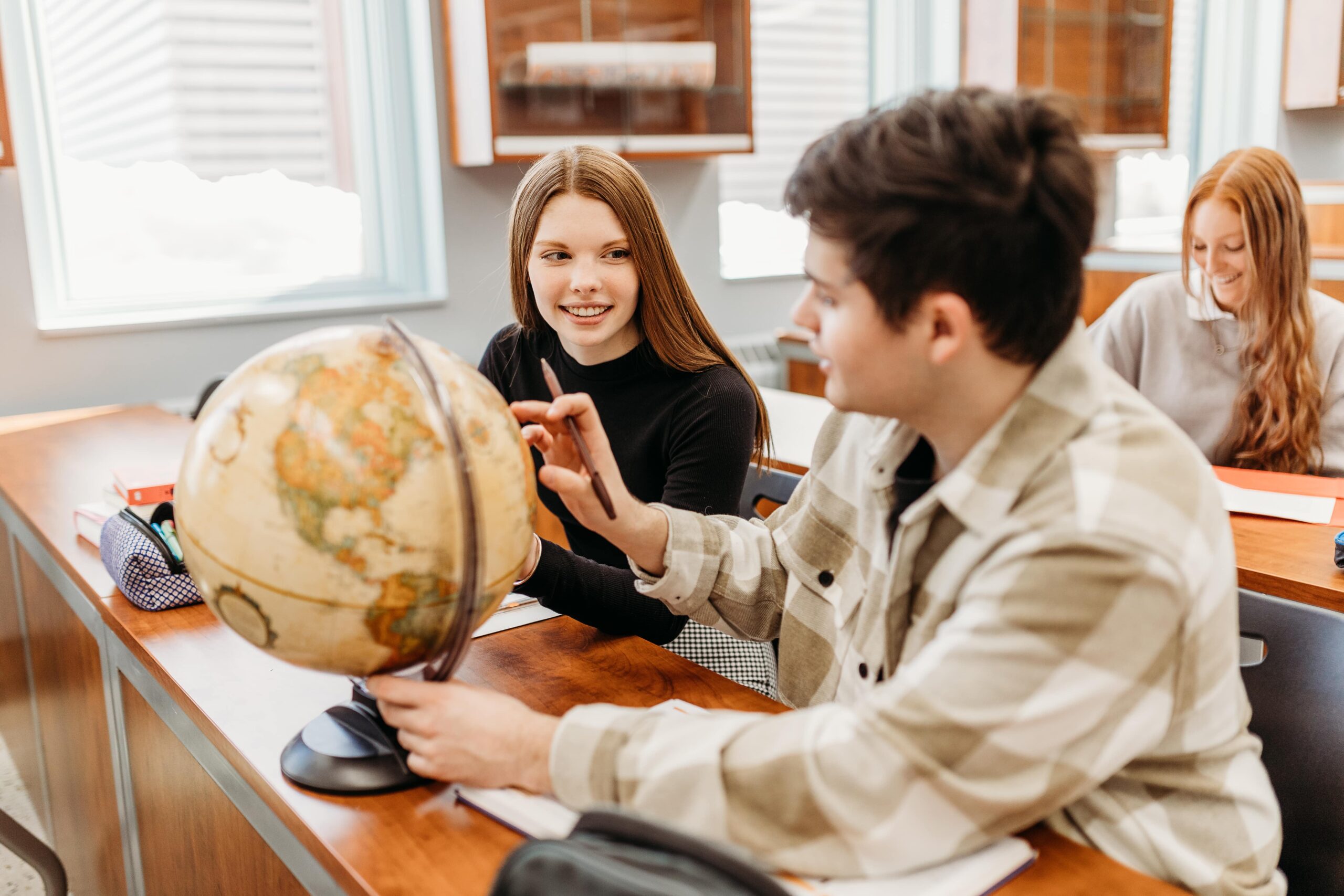 Trois étudiants dans une classe consultent un globe terrestre.