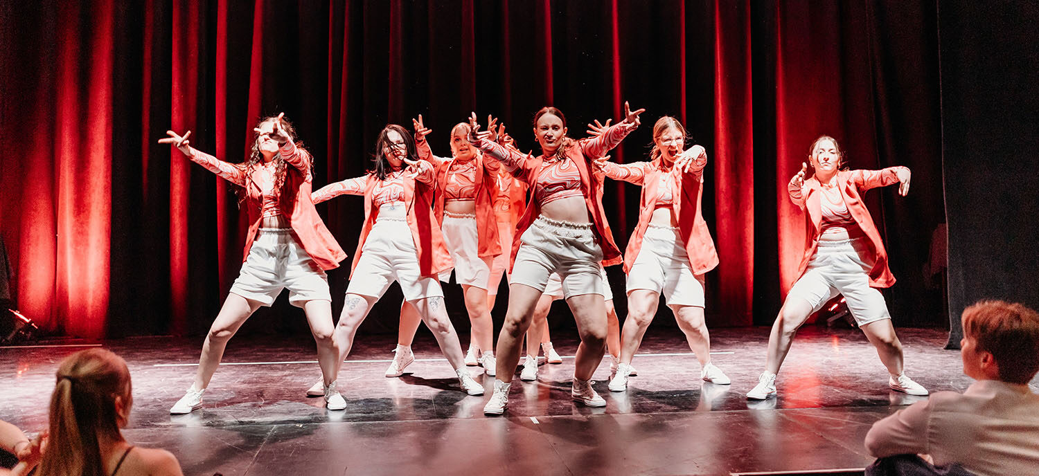 Photo croquée sur le vif d'une troupe de dance en plein spectacle. Les artistes portent des vêtements urbains hip-hop rouge et beige.