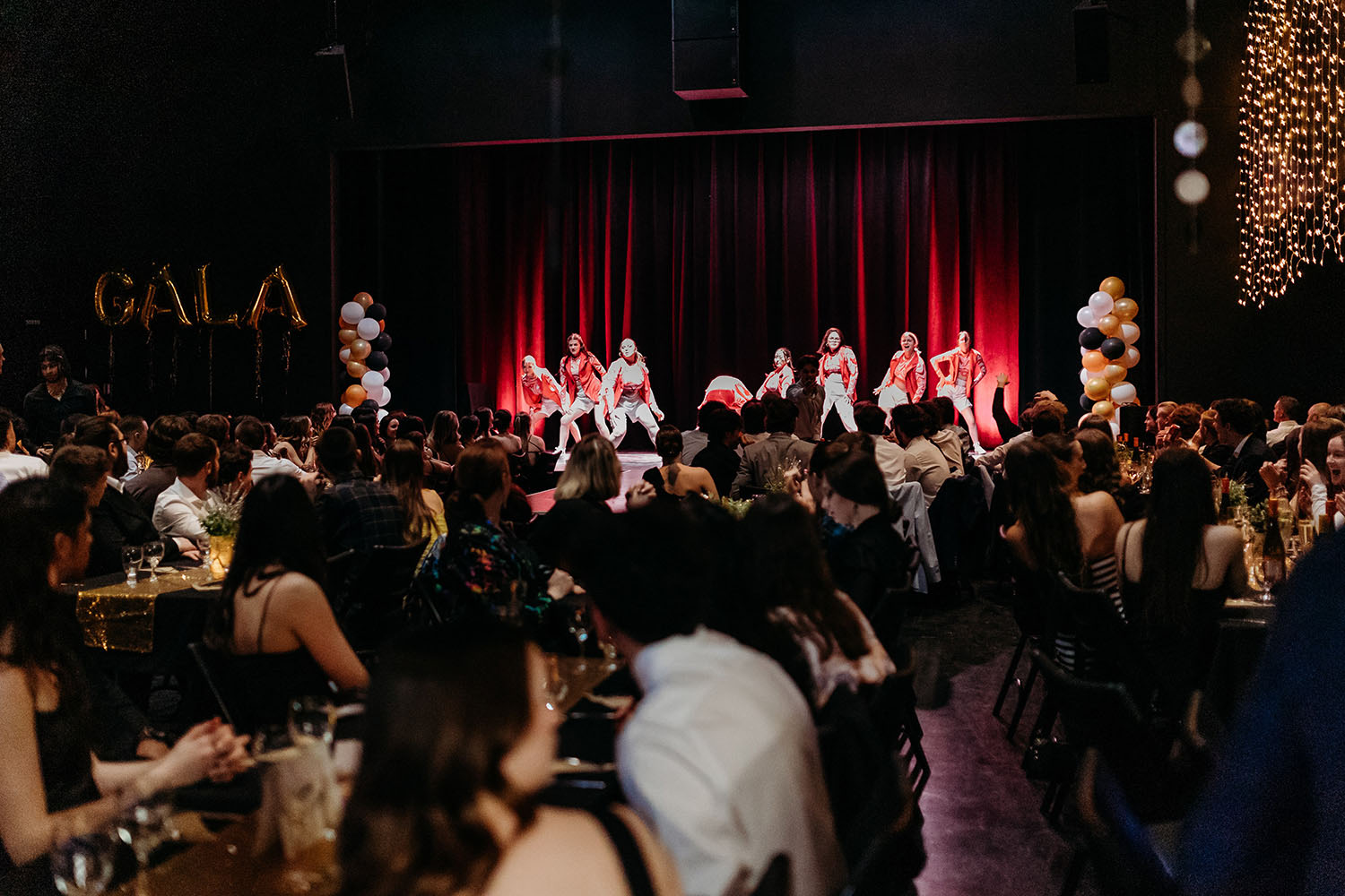 Photo plan large d'une salle bondée assistant à un spectacle d'une troupe de danse. Les artistes portent des vêtements urbains hip-hop rouge et beige.