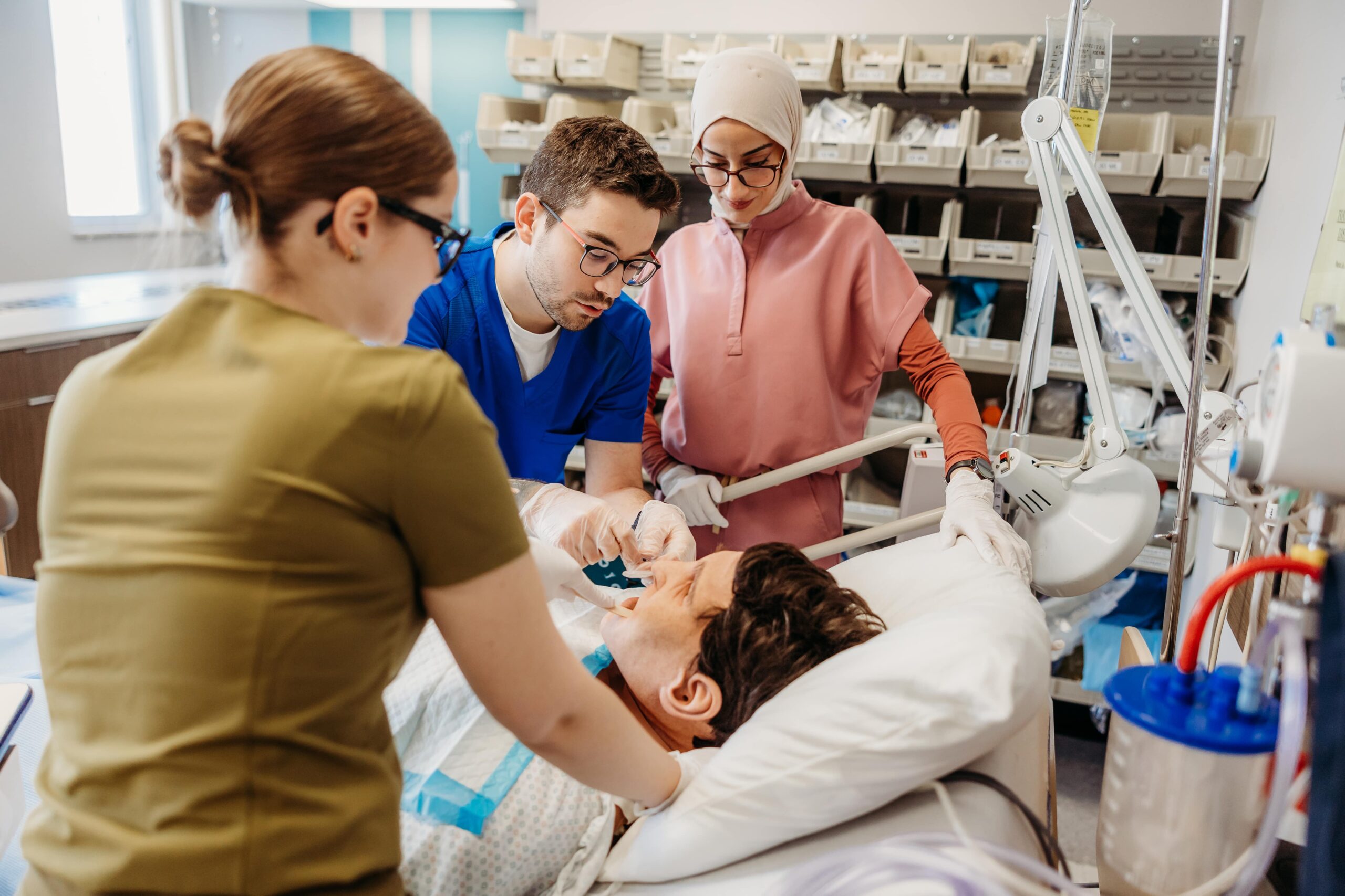 Trois jeunes professionnels en santé sont au dessus d'un patient couché sur une civière dans un contexte d'apprentissage en intervention médicale.