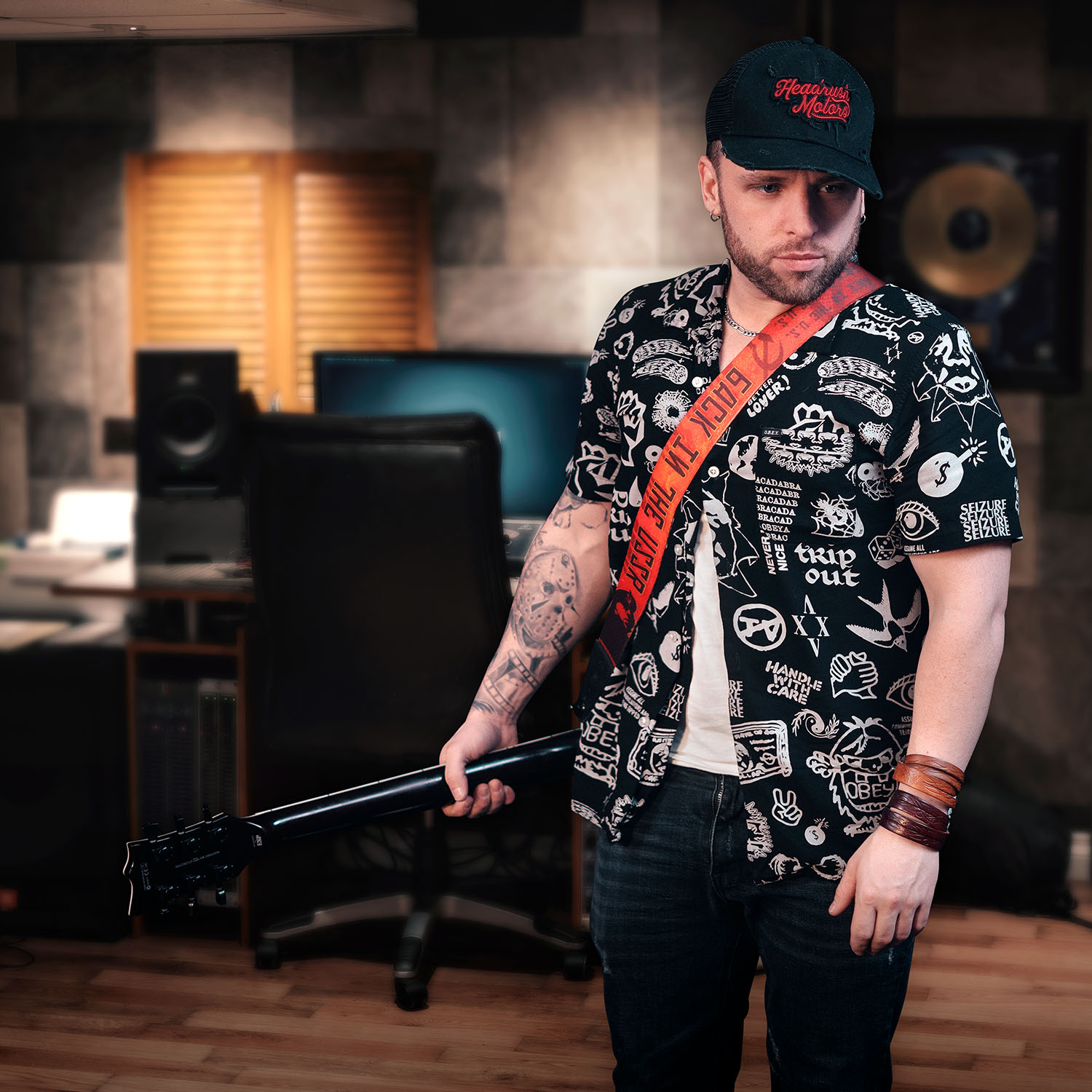 Un jeune artiste de la relève avec une guitare à la main dans un environnement de studio. Il porte une casquette et une chemise, ainsi que plusieurs bracelets.