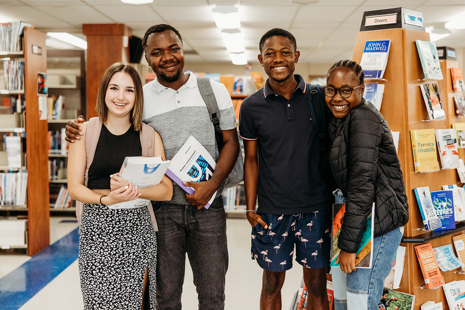 Des étudiants sourient à la caméra dans la bibliothèque.