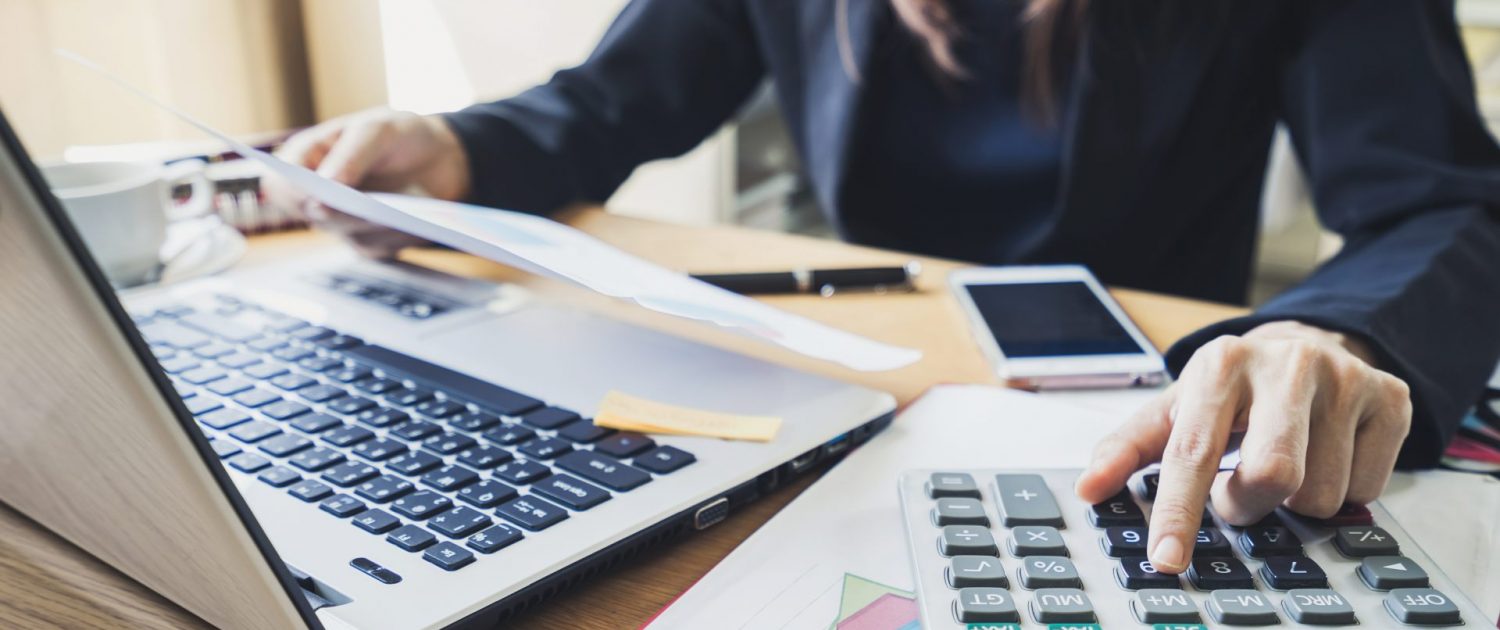 Une femme utilise une calculatrice devant son ordinateur.